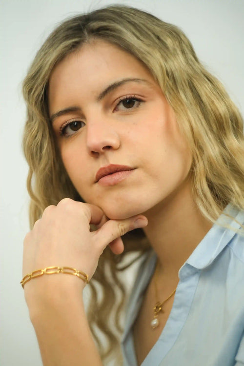 Woman with blonde hair wearing a light blue shirt and gold jewelry against a white background