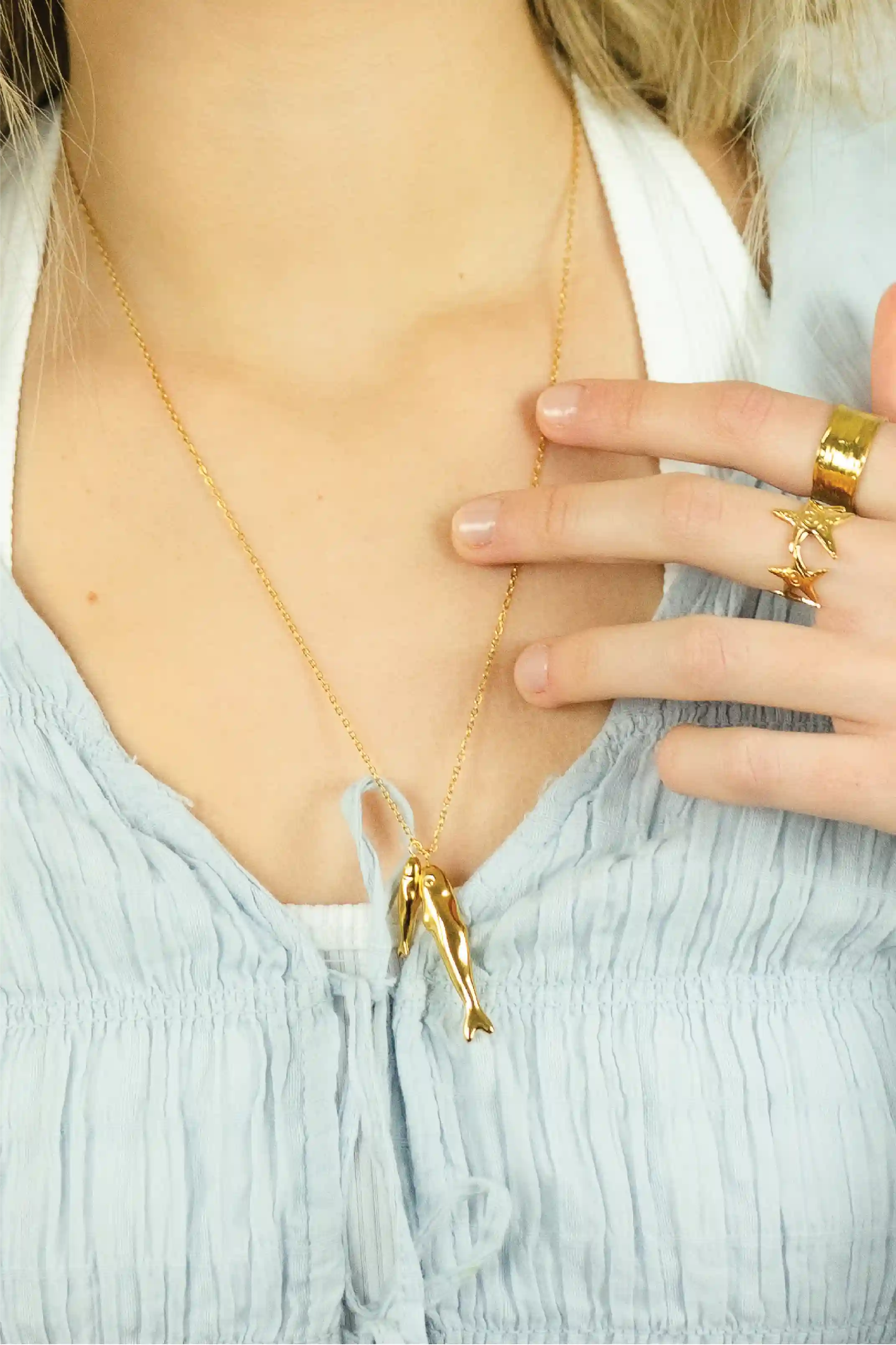 Gold necklace with a unique pendant worn by a person in a light blue top.