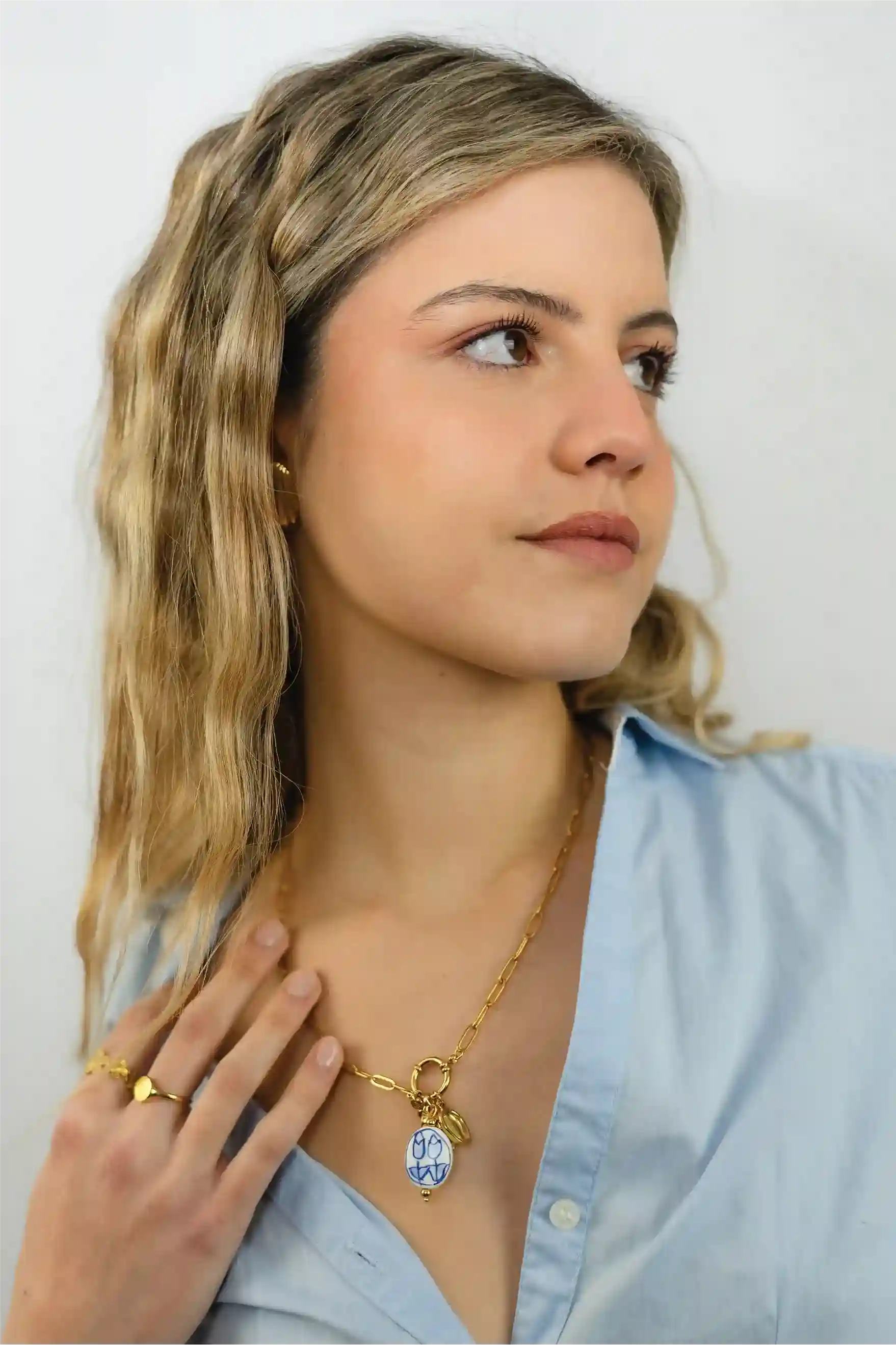 Woman wearing a gold necklace with a blue pendant against a plain background