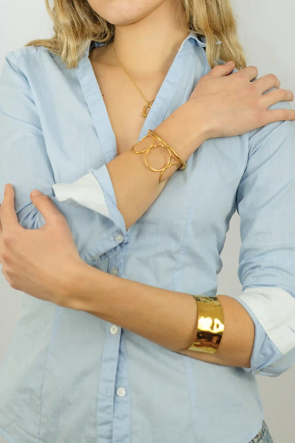 Person wearing gold bracelets on a light blue shirt