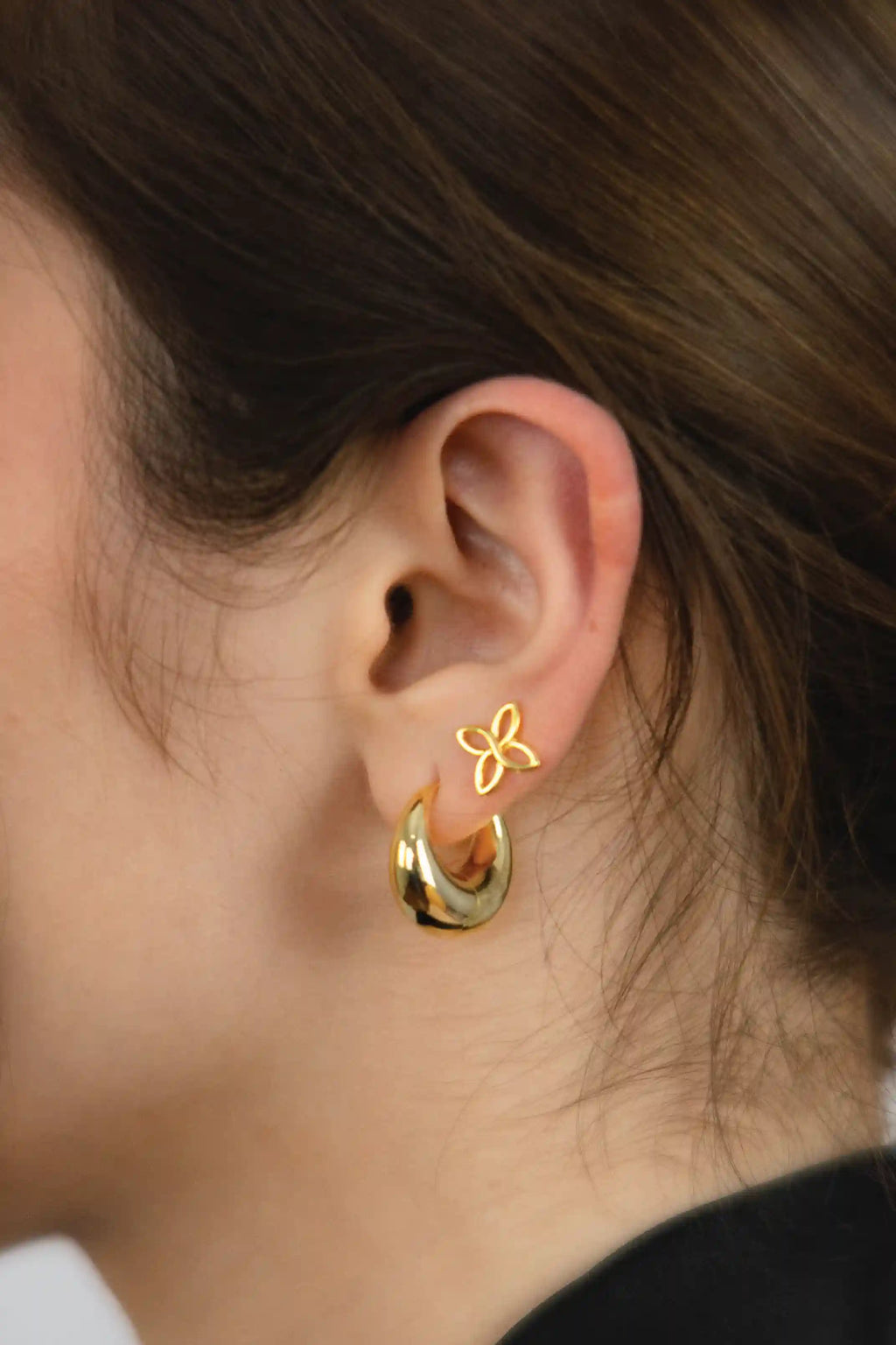 Gold hoop earrings with a butterfly detail worn by a person.