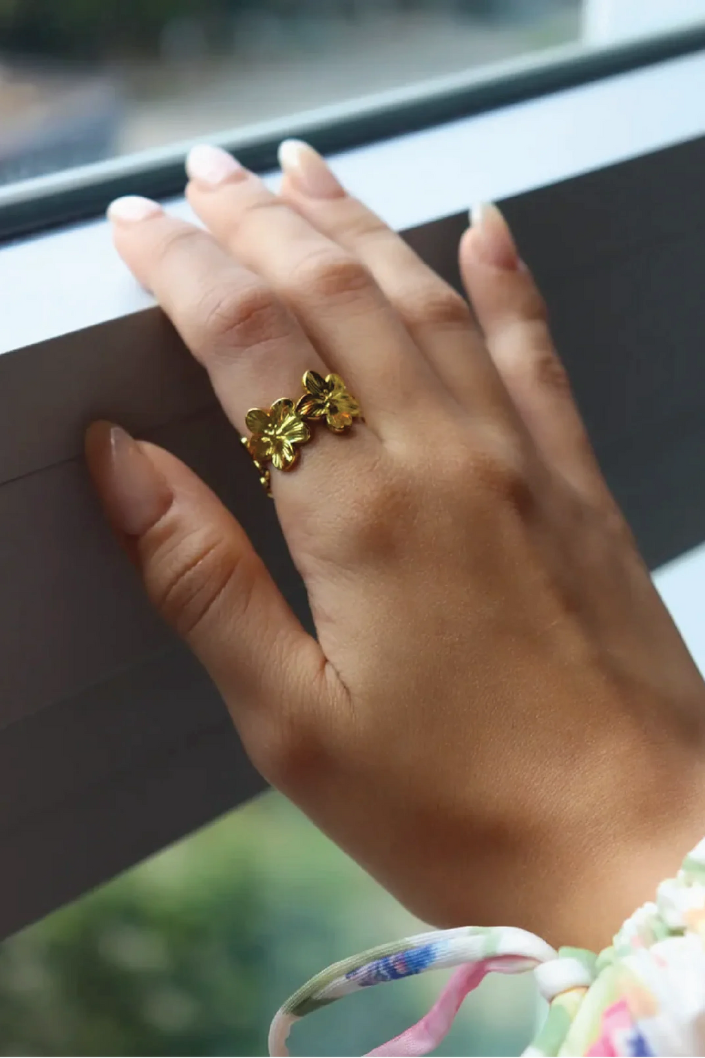 Hand wearing a gold floral ring with a blurred background