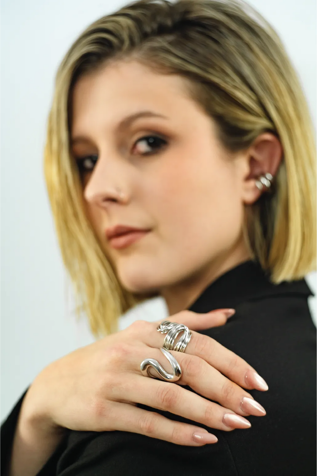 Woman wearing multiple silver rings on a plain background