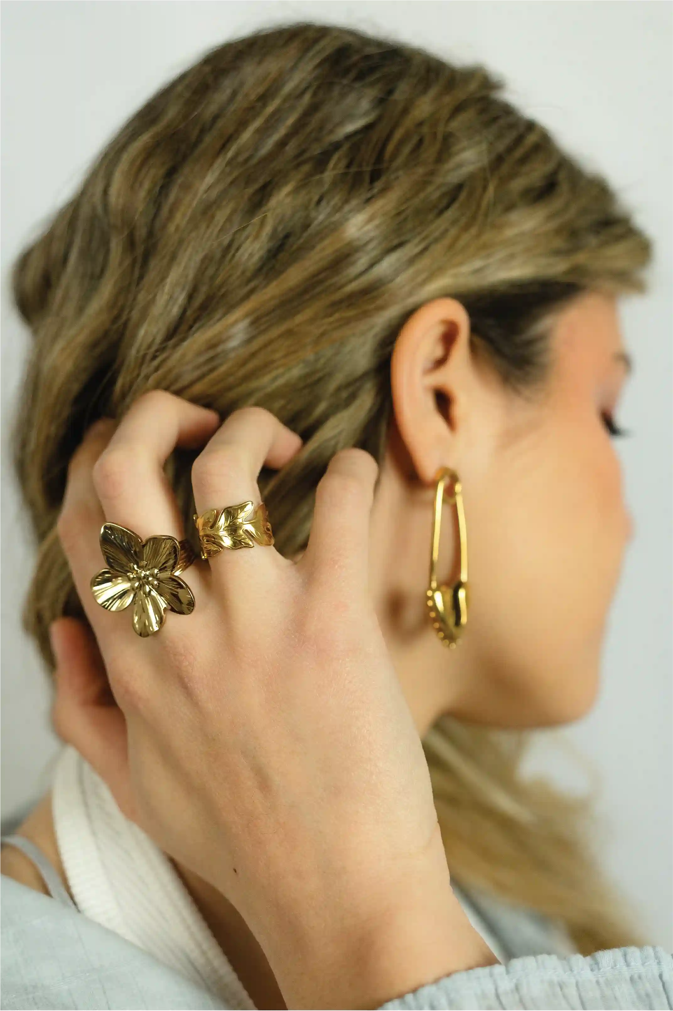 Person wearing gold hoop earrings and rings, adjusting hair with a neutral background