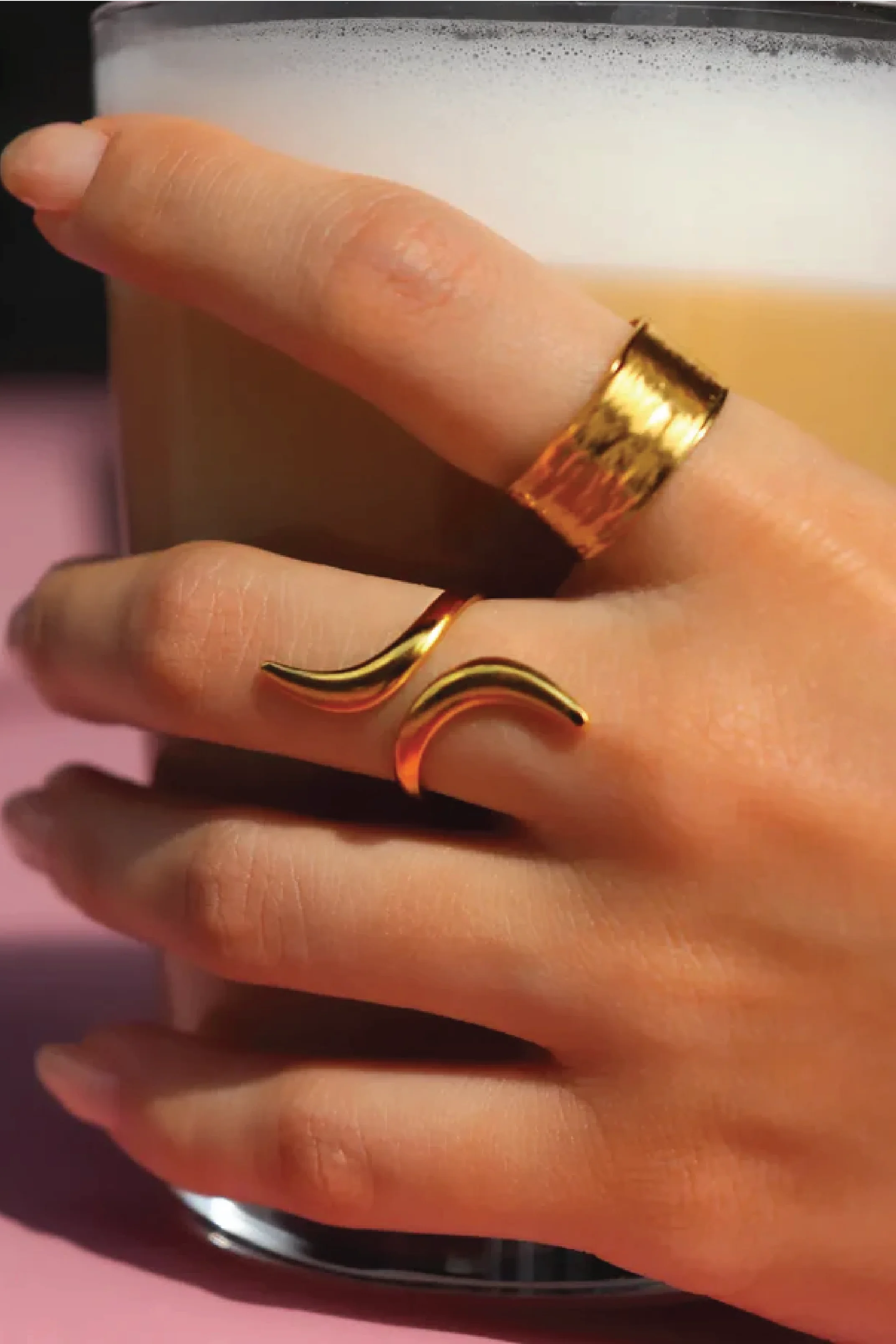 Hand wearing a gold ring with a unique design, holding a cup of coffee.