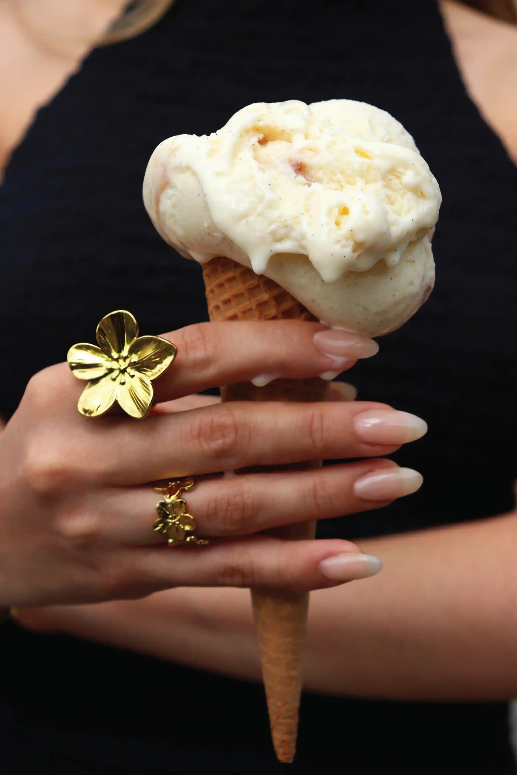 Ice cream cone held by a hand with gold rings, against a black background