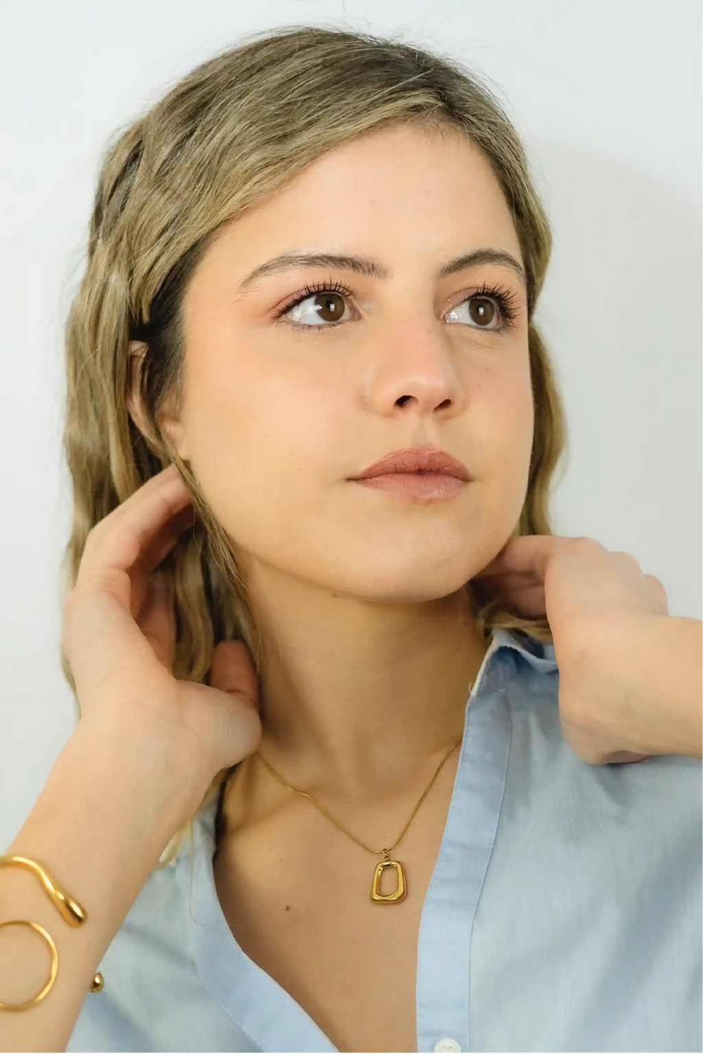 Woman wearing a gold necklace with a plain background