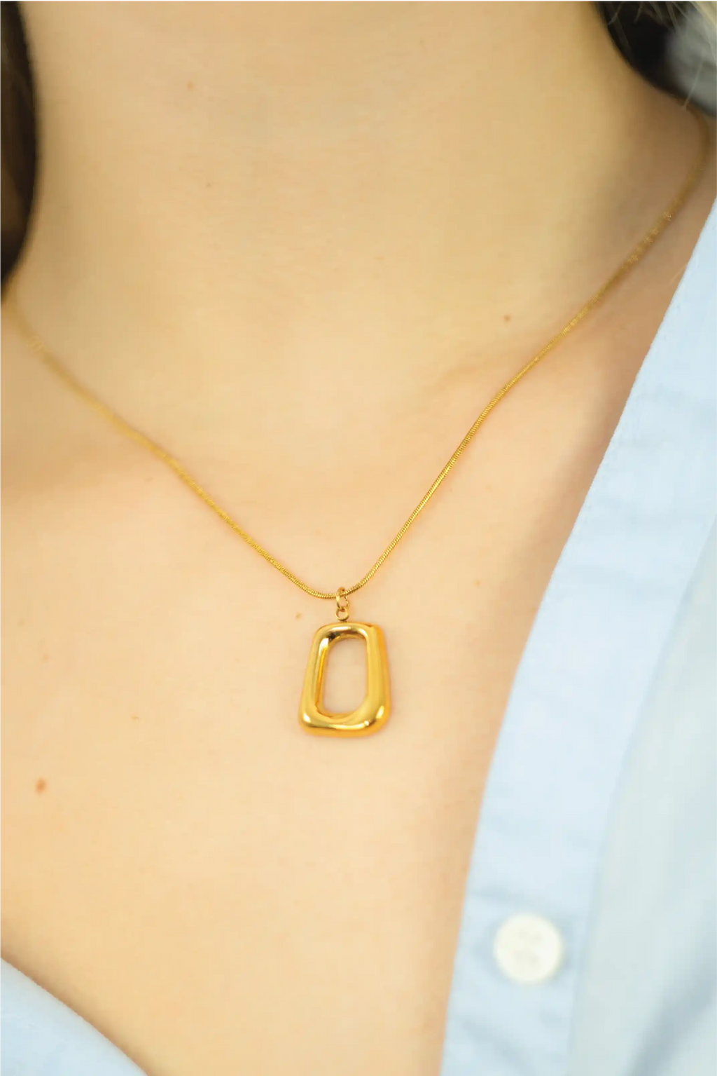 Gold necklace with a unique pendant on a person wearing a light blue shirt.