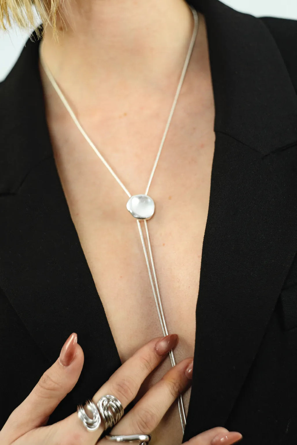 Silver necklace with a pendant worn by a person against a black background
