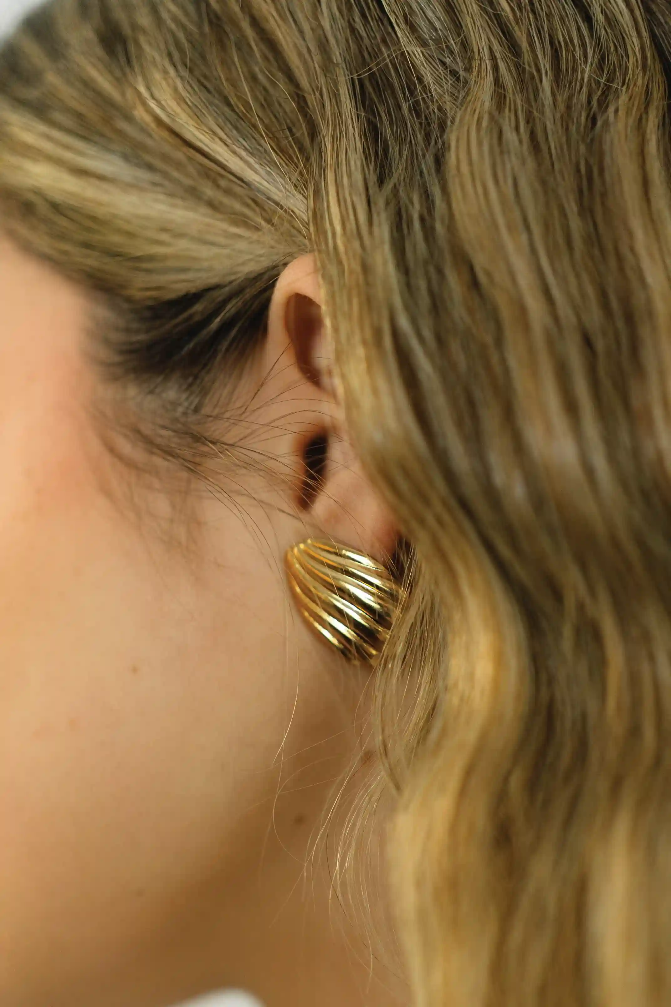 Close-up of a person wearing a gold earring with blonde hair.