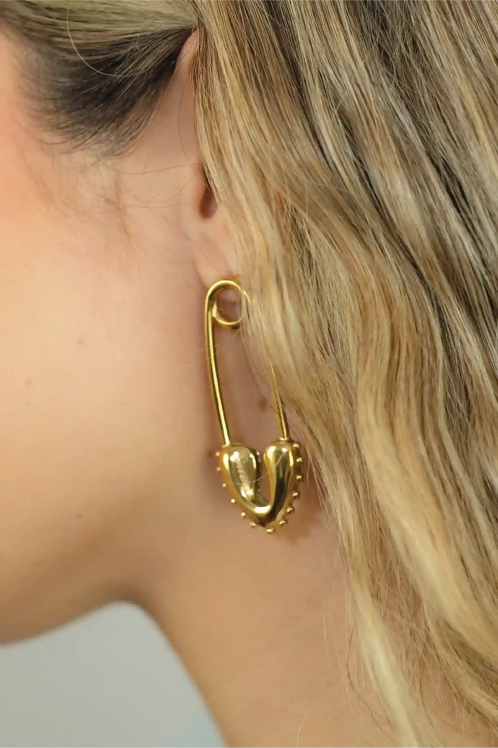 Gold safety pin earring worn by a person with blonde hair.