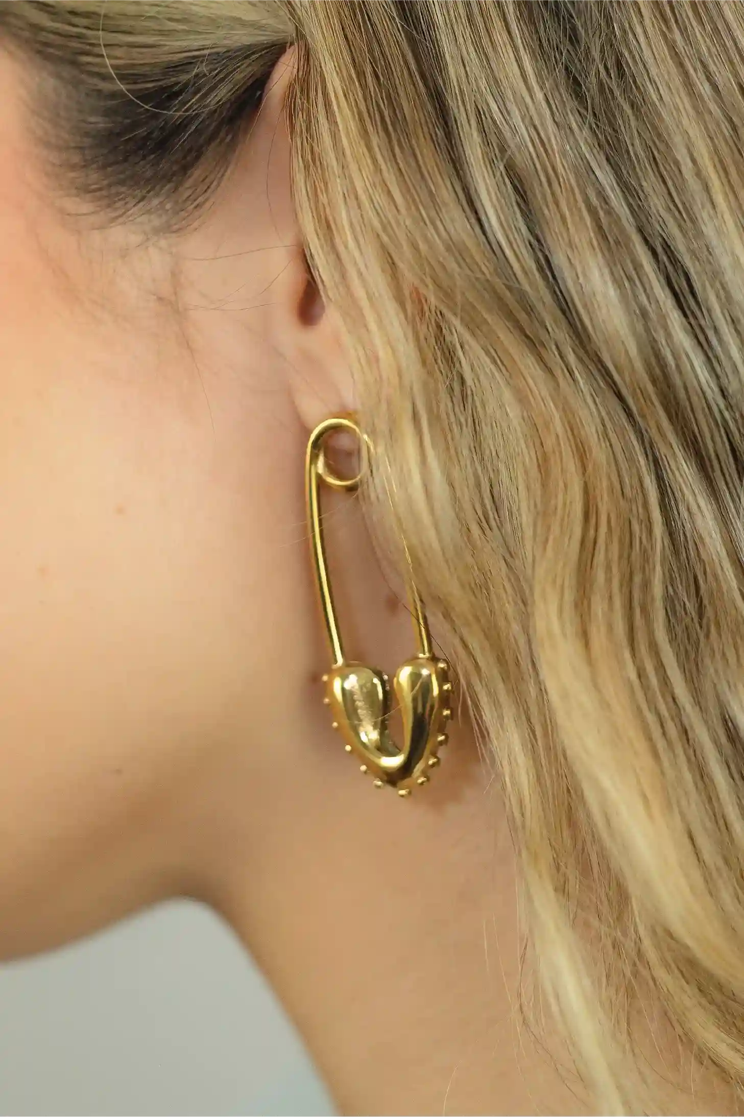 Gold safety pin earring worn by a person with blonde hair.