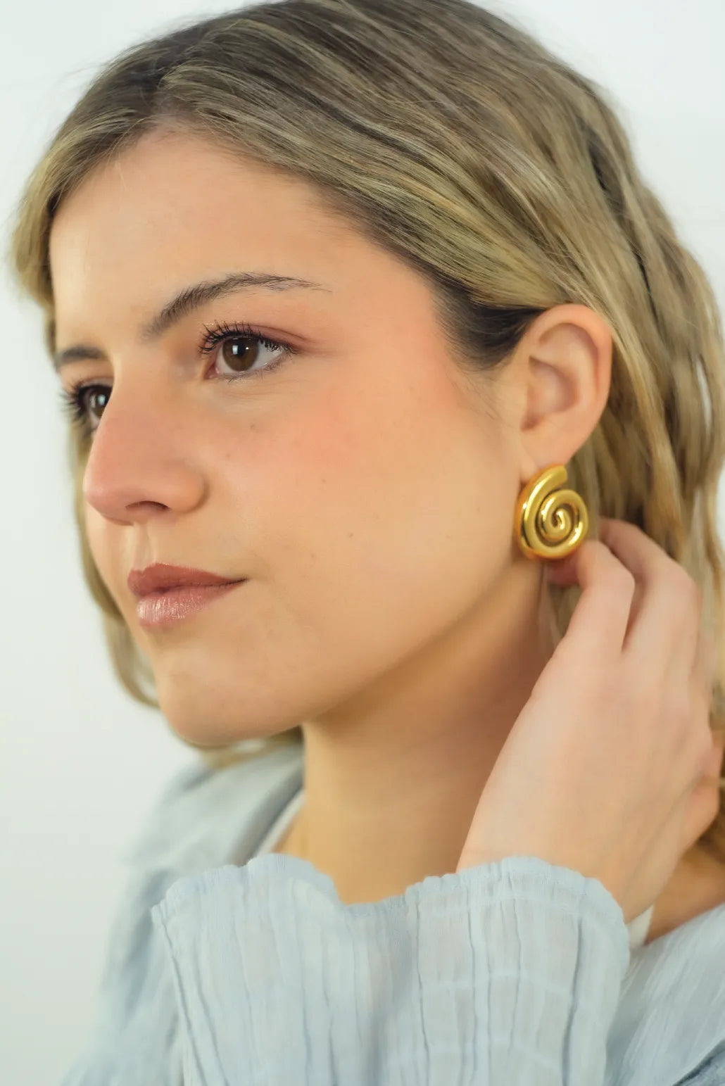 Woman wearing a gold spiral earring against a white background