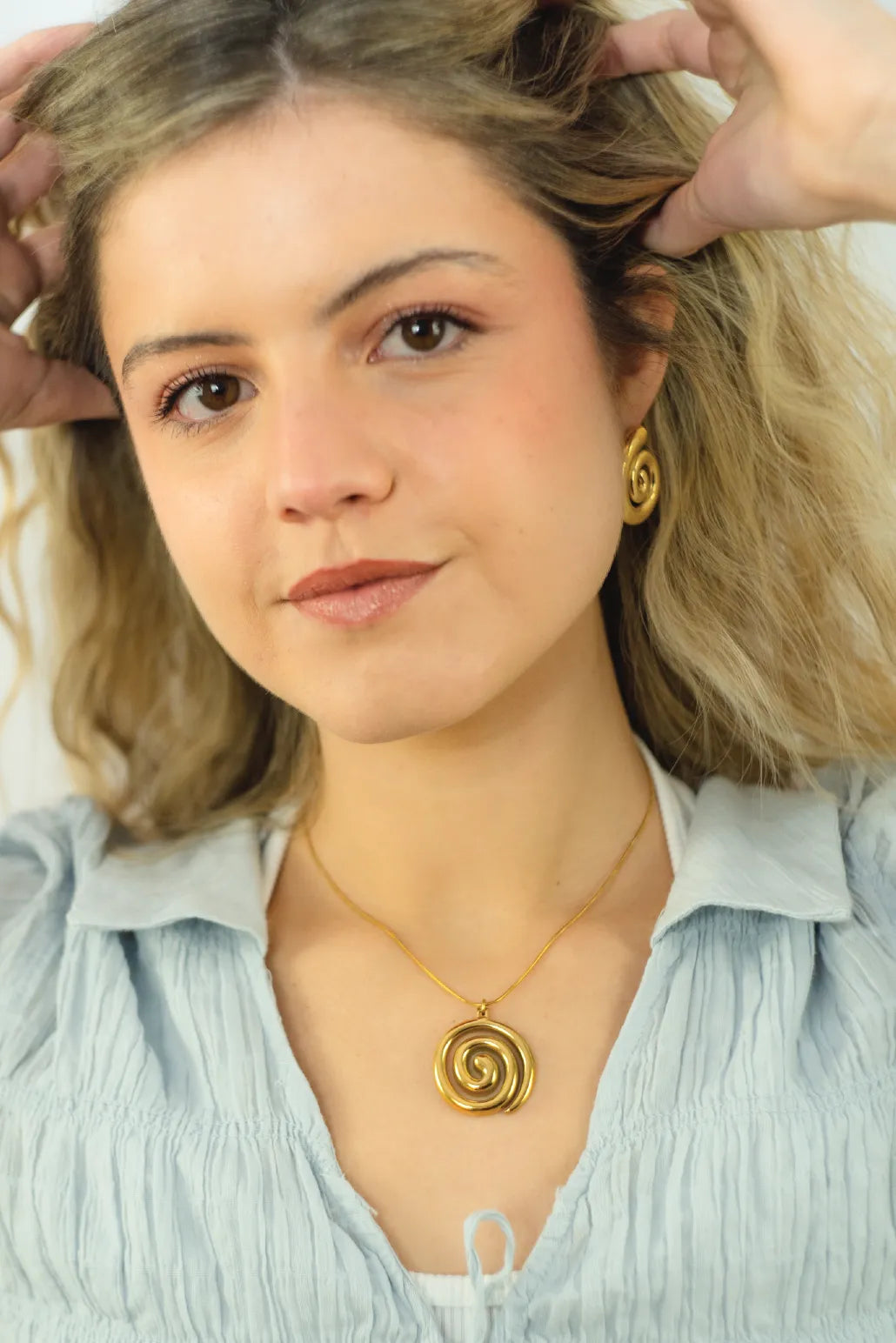 Woman wearing a gold spiral necklace and earrings, with hands adjusting her hair.