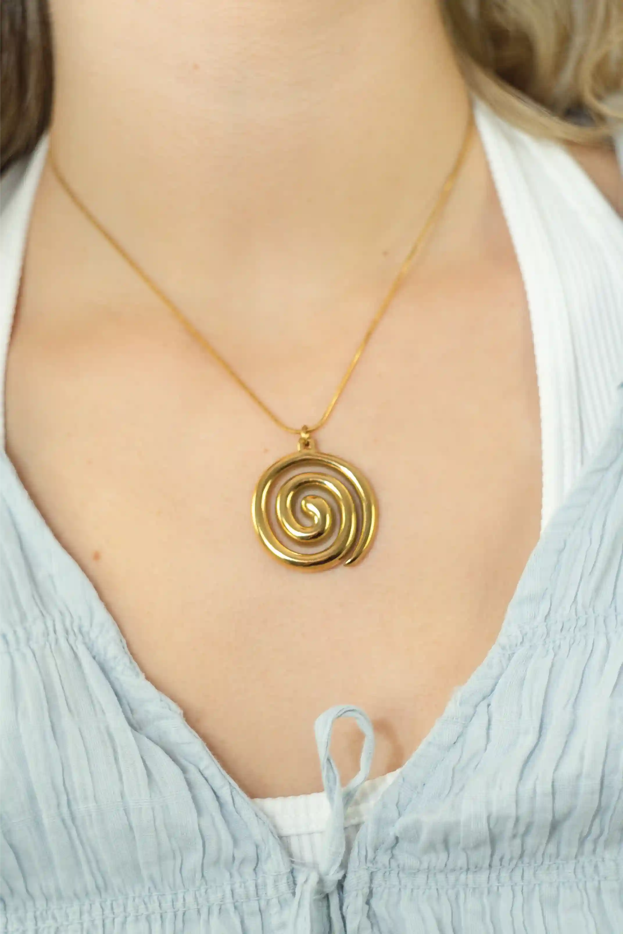 Gold spiral pendant necklace on a person wearing a light blue top.